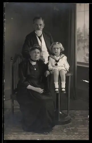 Foto-AK Josi mit seiner Familie im Matrosenanzug, Studiokulisse eines Raumes mit Fenster