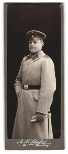 Fotografie M. B. Schultz, Flensburg, Einjährig-Freiwilliger Beckmann im Uniformmantel mit Schirmmütze und Seitenwaffe