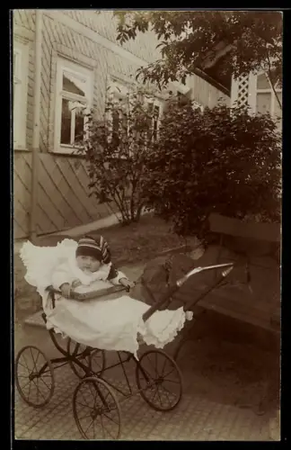 Foto-AK Kleinkind mit Zipfelmütze im Kinderwagen in einem Hof