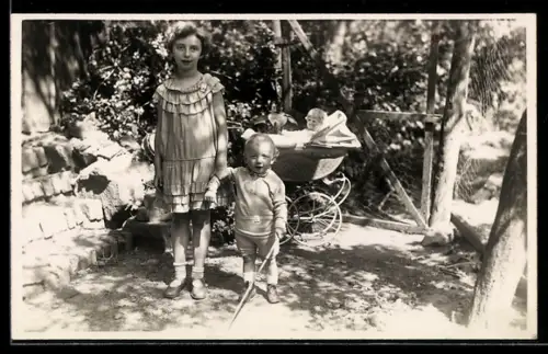 Foto-AK Mädchen u. kleiner Junge mit Puppe im Kinderwagen in einem Garten