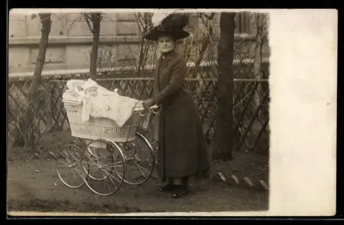 Foto-AK Dame im Mantel mit Kleinkind im Kinderwagen neben einem Jägerzaun