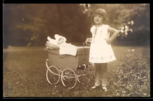 Foto-AK Kleines Mädchen im Sommerkleid mit Puppe im Puppenwagen auf einer Rasenfläche