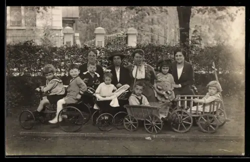 Foto-AK Vier Frauen mit einer gemischten Kindergruppe vor einem grossen Gebäude, Bollerwagen, Spielzeugauto