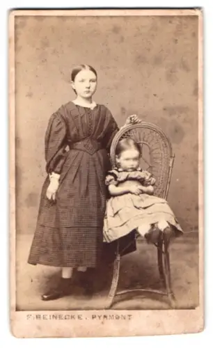 Fotografie F. Reinecke, Pyrmont, junge Mädchen im dunklen Kleid mit ihrer kleinen Schwester auf dem Stuhl
