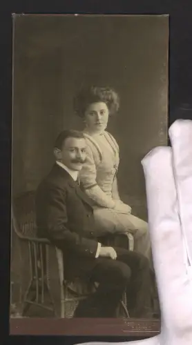 Fotografie Hermann & Klein, Elberfeld, Paar in eleganter Kleidung auf einem Stuhl