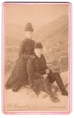 Fotografie G. Gassler, Davos, Ansicht Davos, Paar auf Schlitten im Schneetreiben vor Stadtansicht, Fotomontage