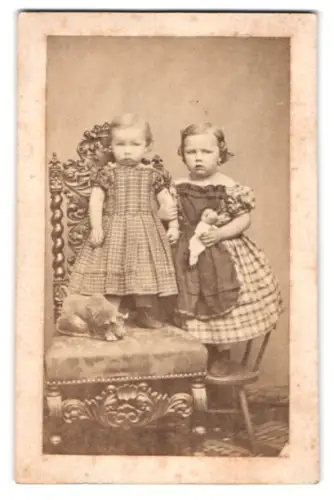 Fotografie unbekannter Fotograf und Ort, kleine Mädchen mit Puppe tragen karierte Kleider