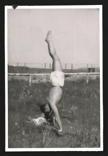 Fotografie Junger Mann in Badehose beim Handstand auf einer Wiese