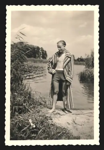 Fotografie Mann in Badehose und mit Bademantel steht an einem Seeufer