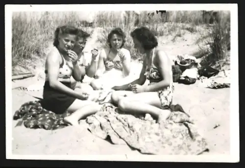 Fotografie Vier Frauen in Badebekleidung sitzen an einem sonnigen Tag am Strand auf Decken