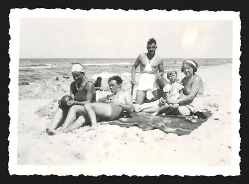 Fotografie Menschengruppe in Badeanzügen und mit Ball geniesst den Tag in unmittelbarer Wassernähe am Strand