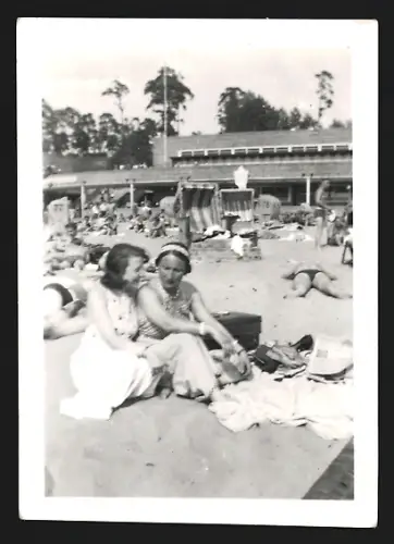 Fotografie Zwei Frauen sitzen in einer Menschenmenge am Strand und geniessen einen sonnigen Tag