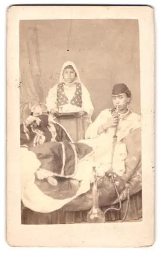 Fotografie arabische Damen in Tracht rauchen Wasserpfeife, Diener im Hintergrund mit Tablett