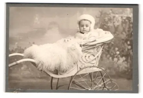 Fotografie unbekannter Fotograf und Ort, Kind mit Fell bedeckt im Kinderwagen