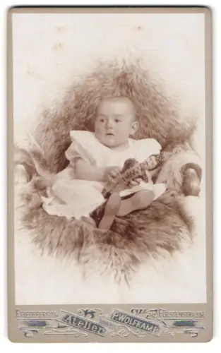 Fotografie P. Wolfkamp, Friedeberg /N. M., Fürstenstrasse, Kleinkind mit Spielzeugpuppe auf Fell sitzend