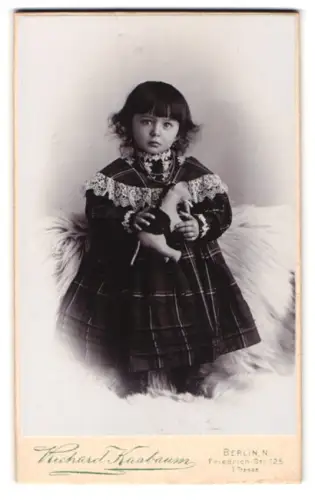 Fotografie Richard Kostbaum, Berlin, Friedrich-Str. 125, Kind in kariertem Kleid mit Plüschelefant