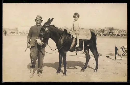 Foto-AK Kleines Kind beim Eselritt am Strand, mit Führer u. Ortspanorama