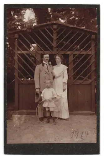 Fotografie unbekannter Fotograf und Ort, Familie im Garten vor Holzlaube