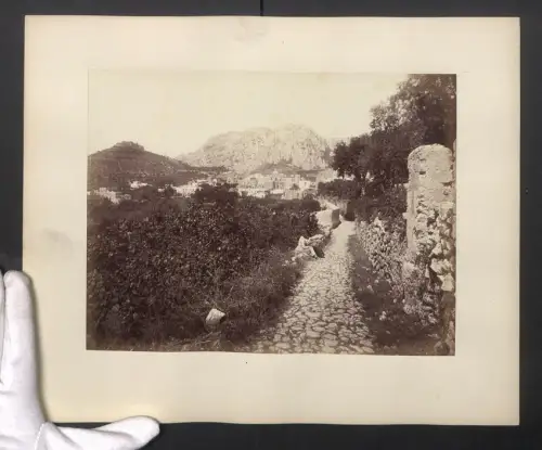Fotografie unbekannter Fotograf, Ansicht Capri, Dame mit Korb am Rand eines steinernen Weges, Blick auf die Berge