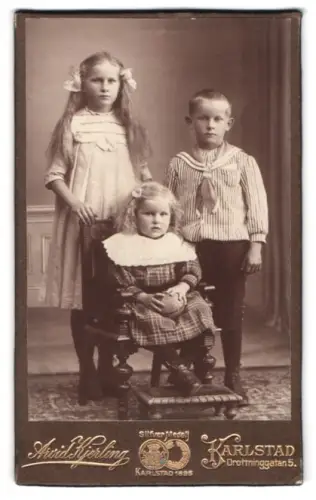 Fotografie A. Kjerling, Karlstad, Drottninggatan 5, Zwei Mädchen mit Schleifen in den Haaren und ihr Bruder