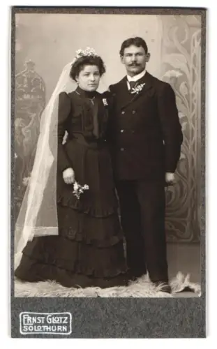 Fotografie Ernst Glutz, Solothurn, Elegantes Hochzeitspaar mit Blumen und Schleier, Braut in schwarzem Kleid