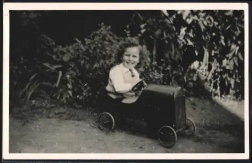 Fotografie Spielzeug-Auto, glückliches Mädchen im Tretauto / Draisine sitzend