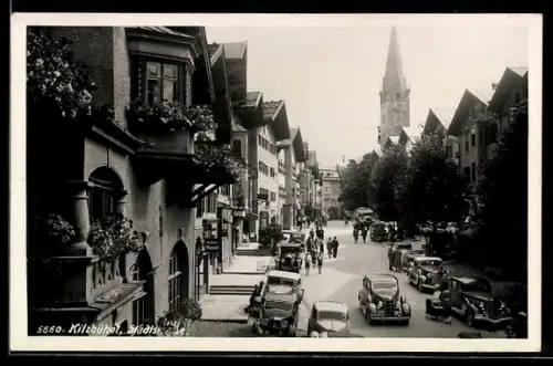 AK Kitzbühel, die Stadtstrasse mit Kirche, parkende Autos, Geschäft Julius Meinl, Weinstube und Gasthof
