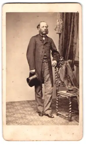 Fotografie P. Schindler, Regensburg, Mann mit Zylinder steht neben einem Stuhl