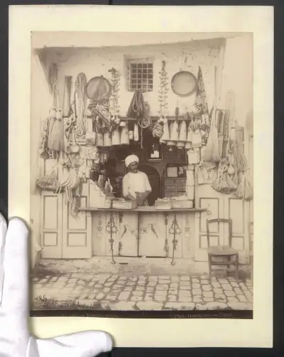 Fotografie Garrigues, Tunis, arabischer Gemischtwaren Händler in seinem Geschäft, Epicier arabe, Tracht, 24 x 31cm