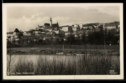 AK Enns /Ob. Öst., Stadtsilhouette mit Kirche, Flussufer im Vordergrund