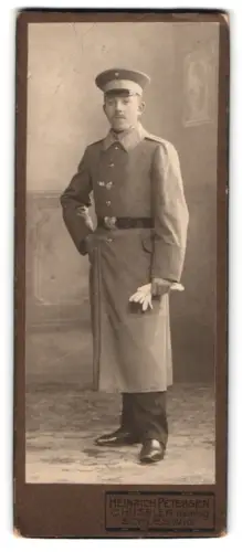 Fotografie Heinrich Petersen, Schleswig, Soldat in Uniformmantel mit Schirmmütze, Sept. 1912