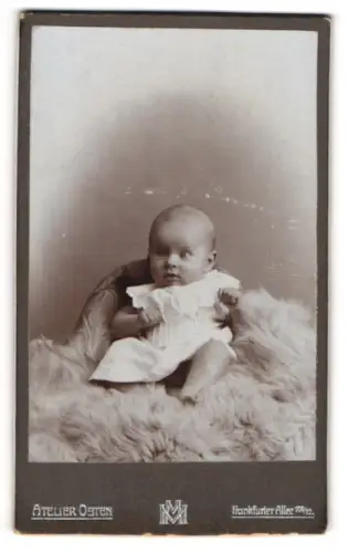 Fotografie Atelier Osten, Berlin, Portrait niedliches Baby im weissen Hemd auf Fell sitzend