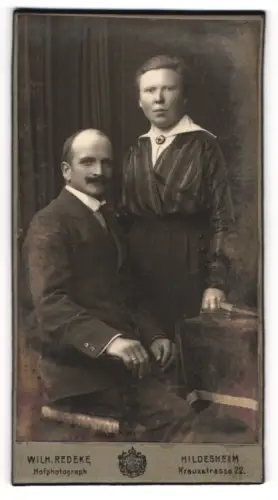 Fotografie Wilh. Redeke, Hildesheim, Portrait bürgerliches Paar in modischer Kleidung am Tisch