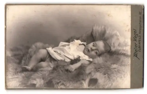 Fotografie Atelier Kegel, Elberfeld, süsses Baby im weissen Kleidchen auf Fell liegend
