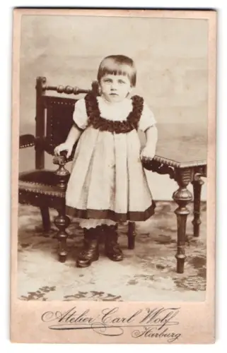 Fotografie Carl Wolf, Harburg, Kind in Kleid vor Stuhl