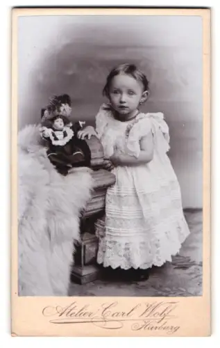 Fotografie Carl Wolf, Harburg, Kleinkind im weissen Kleid mit einer Spielzeugpuppe