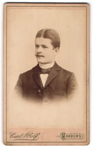 Fotografie Carl Wolf, Harburg, Portrait junger Mann im Anzug mit Fliege und Zwirbelbart