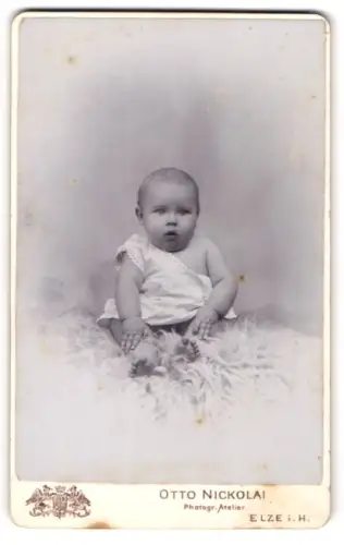 Fotografie Otto Nickolai, Elze i. H., Portrait niedliches Baby im weissen Hemd auf Fell sitzend