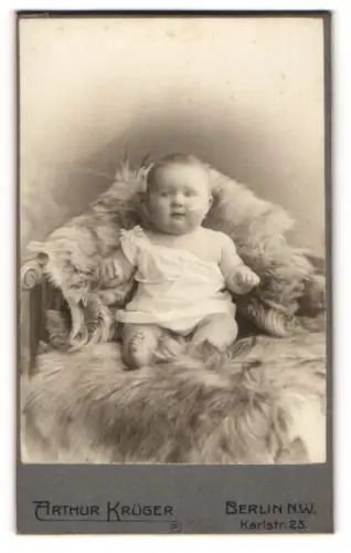 Fotografie Arthur Krüger, Berlin-NW, Portrait niedliches Baby im weissen Hemd auf Fell sitzend