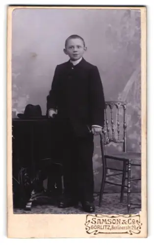 Fotografie Samson & Co., Görlitz, Berlinerstr. 29, Junge im Anzug mit Hut auf Tisch