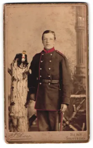Fotografie P. Does, Solothurn, Bahnhofstrasse 209, Porträt eines jungen Soldaten in Uniform mit Helm, handkoloriert