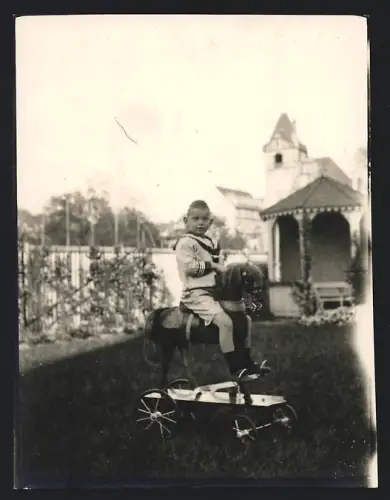 Fotografie Knabe im matrosenanzug auf Spielzeug mit Rädern sitzend