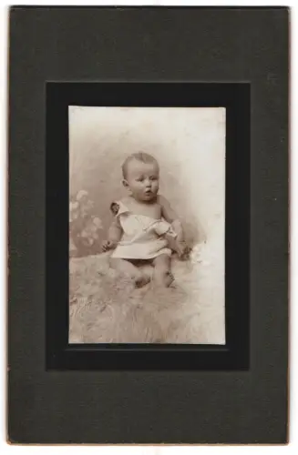 Fotografie unbekannter Fotograf und Ort, Portrait niedliches Baby im weissen Hemd auf Fell sitzend