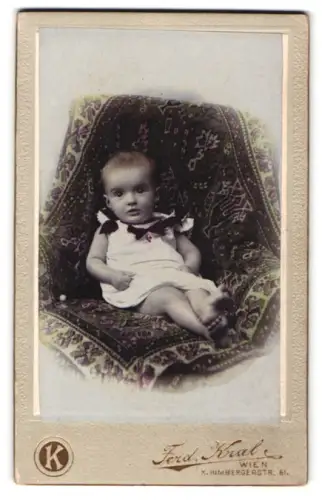 Fotografie Ferd. Kral, Wien, Himbergerstr. 61, Kleinkind auf gemustertem Teppich, handkoloriert