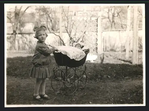 Fotografie Mädchen im Sonntagskleid schiebt Baby im Kinderwagen umher