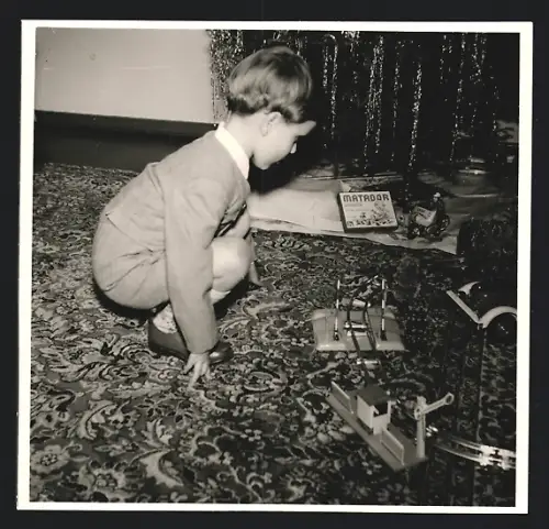 Fotografie Weihnachten, Knabe mit Spielzeug, Blechauto 6 Modell-Eisenbahn neben dem Weihnachtsbaum
