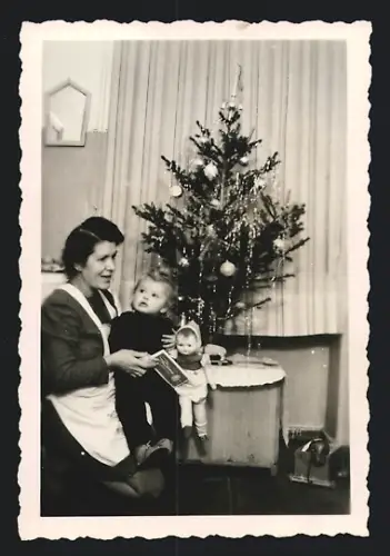 Fotografie Weihnachten, Hausfrau mit Baby und Puppe neben dem Weihnachtsbaum