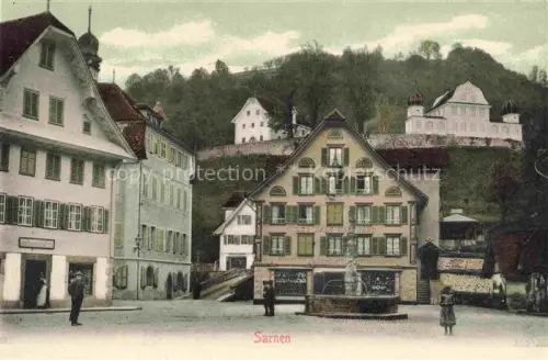 AK / Ansichtskarte Sarnen Obwalden OW Dorfplatz Brunnen Haeuser Kapelle Huegel Geschaefte Passanten