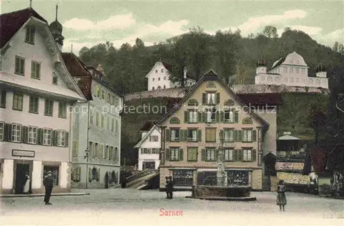 AK / Ansichtskarte Sarnen Obwalden OW Dorfplatz Brunnen Marktplatz Geschaefte Schloss Huegel Passanten