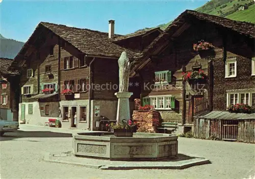 AK / Ansichtskarte Vals Bad Surselva GR Dorfplatz Brunnen Holzhaeuser Chalet Berge Blumen Statue